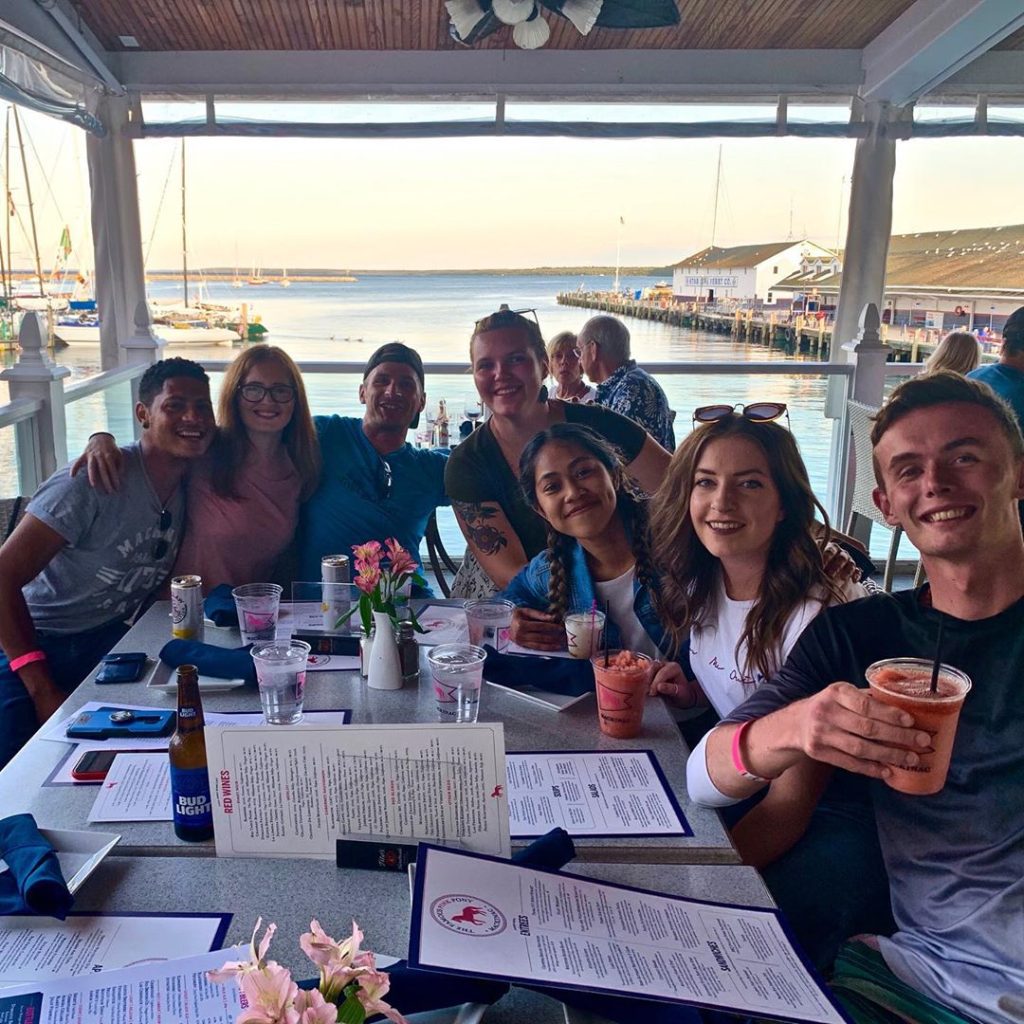 A group of young adults sits around a table in a Mackinac Island restaurant overlooking the water near one of the ferry docks