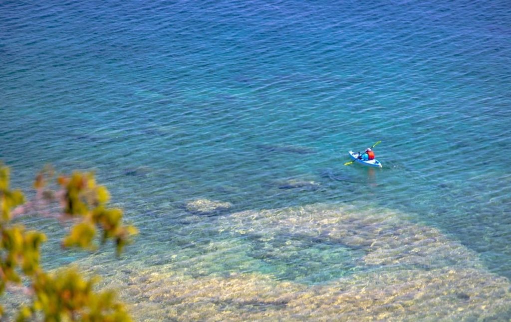 A lone kayaker paddles over the underwater rock maze off Mackinac Island with fall colors in the foreground