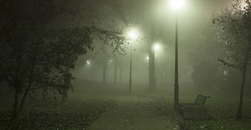 Heavy fog dims streetlights along a sidewalk through the woods on Mackinac Island