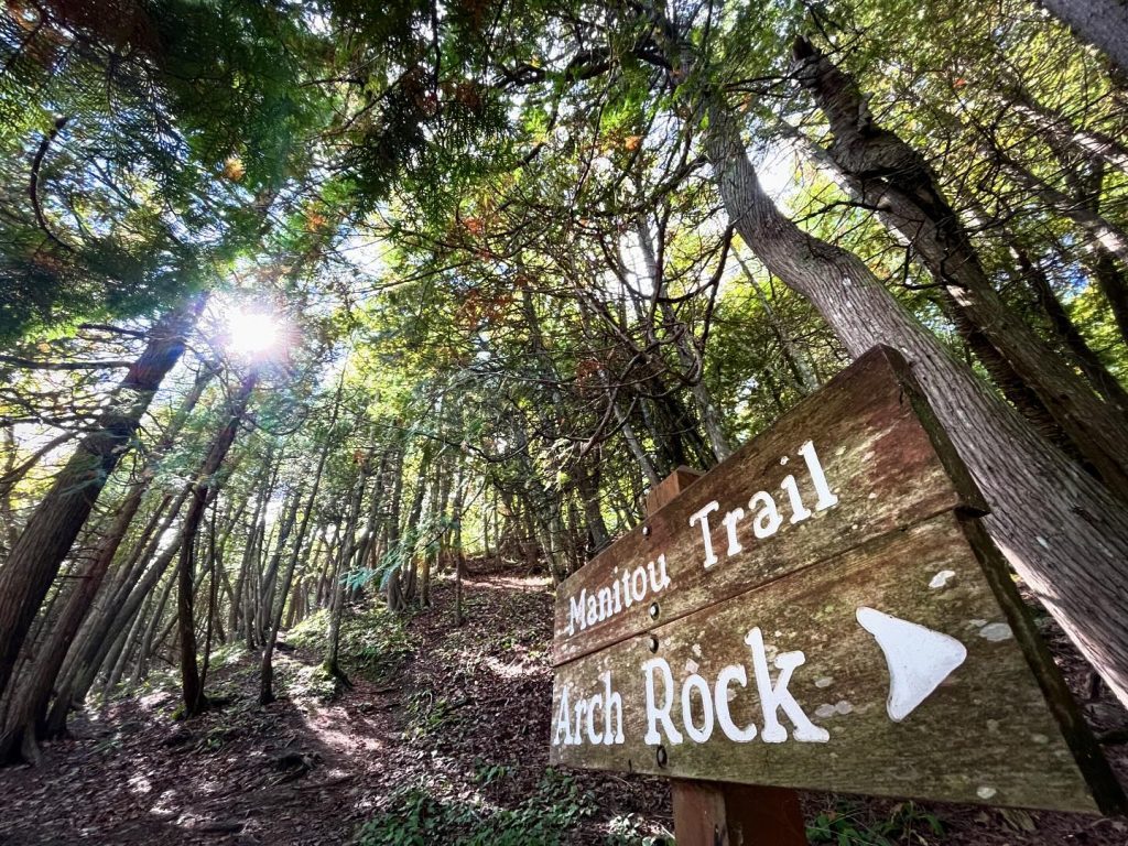 A directional sign in the forest of Mackinac Island State Park pointing to Arch Rock in one direction and Manitou Trail in the other