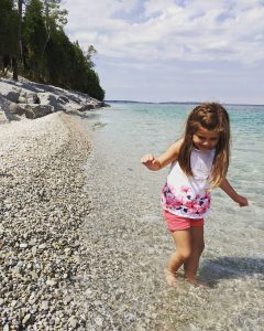 A young girl wades through the water along the rocky shoreline of a Mackinac Island beach