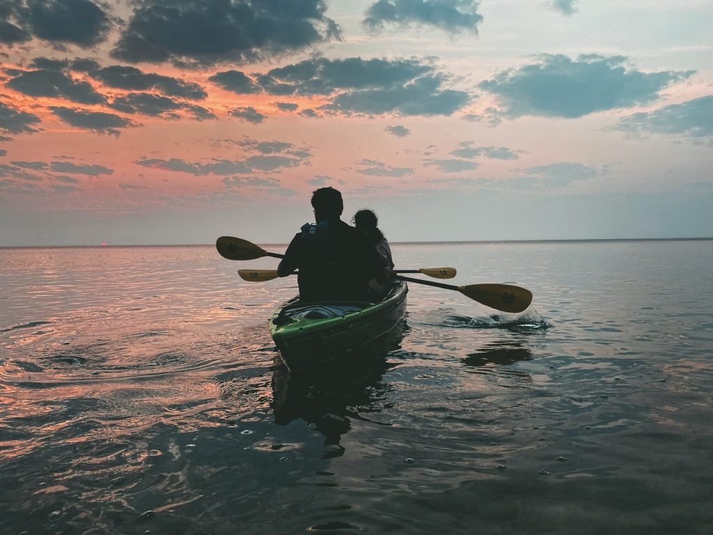 A couple in a tandem kayak paddle in the water around Mackinac Island at sunrise as the light casts a reddish glow