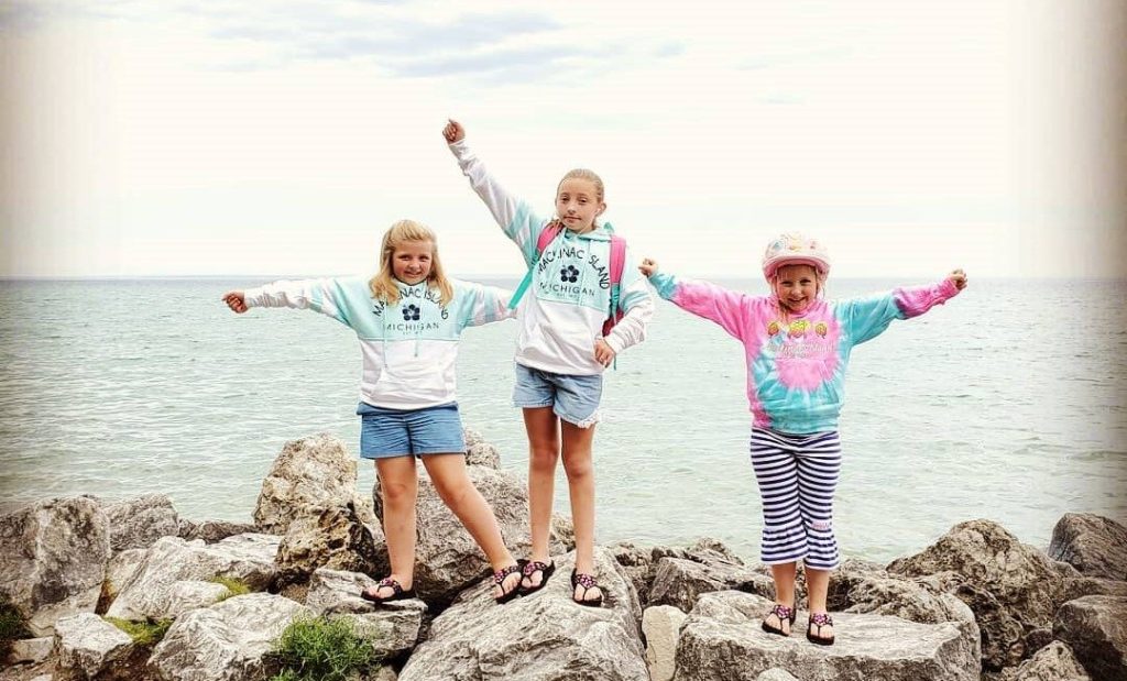 Three young girls stand on rocks along the Mackinac Island shoreline
