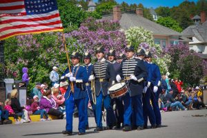 A group of interpretive soldiers walk down the street playing drums and carrying an American flag during a Mackinac Island parade