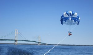 A tandem parasailor floats off the back of a boat near Mackinac Island with the Mackinac Bridge in the background