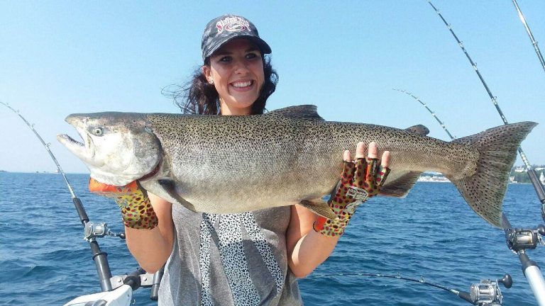 A young woman on a charter fishing boat holds a large fish caught in the water off Mackinac Island