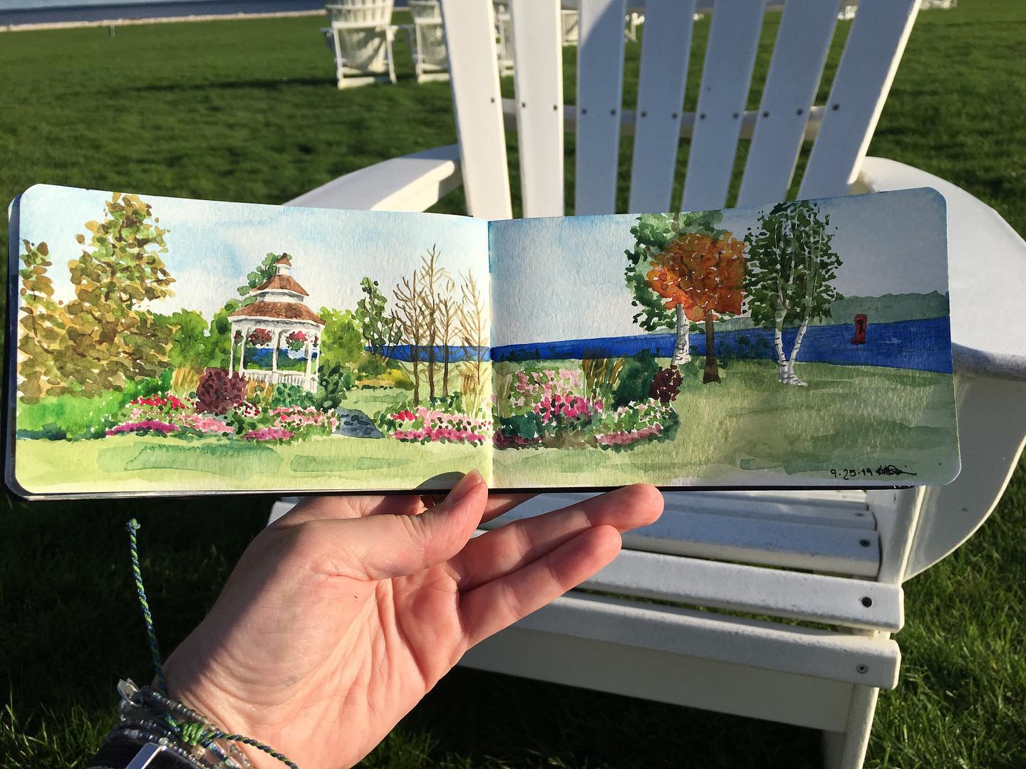 A hand holds a work of art in front of an adirondack chair on the lawn at Mackinac Island's Mission Point Resort