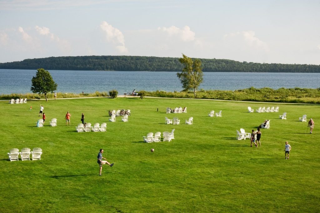 A man kicks a soccer ball while other people mill around Adirondack chairs on the lawn at Mackinac Island’s Mission Point Resort