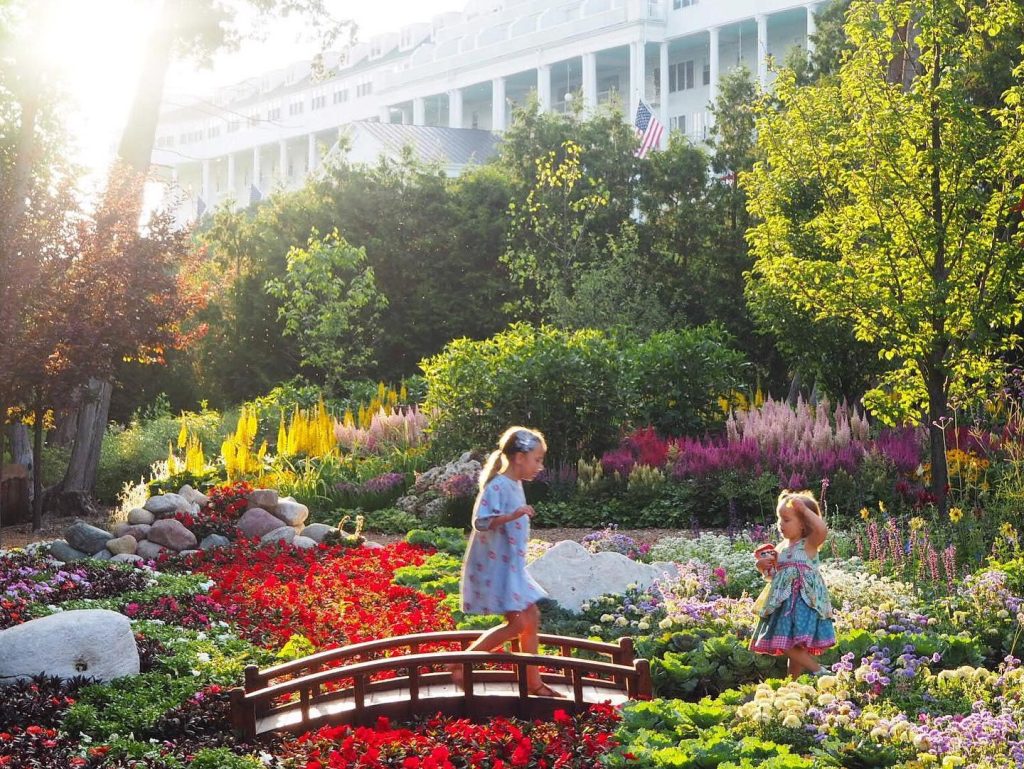 Two little girls cross a bridge in Mackinac Island’s Secret Garden full of colorful flowers below Grand Hotel