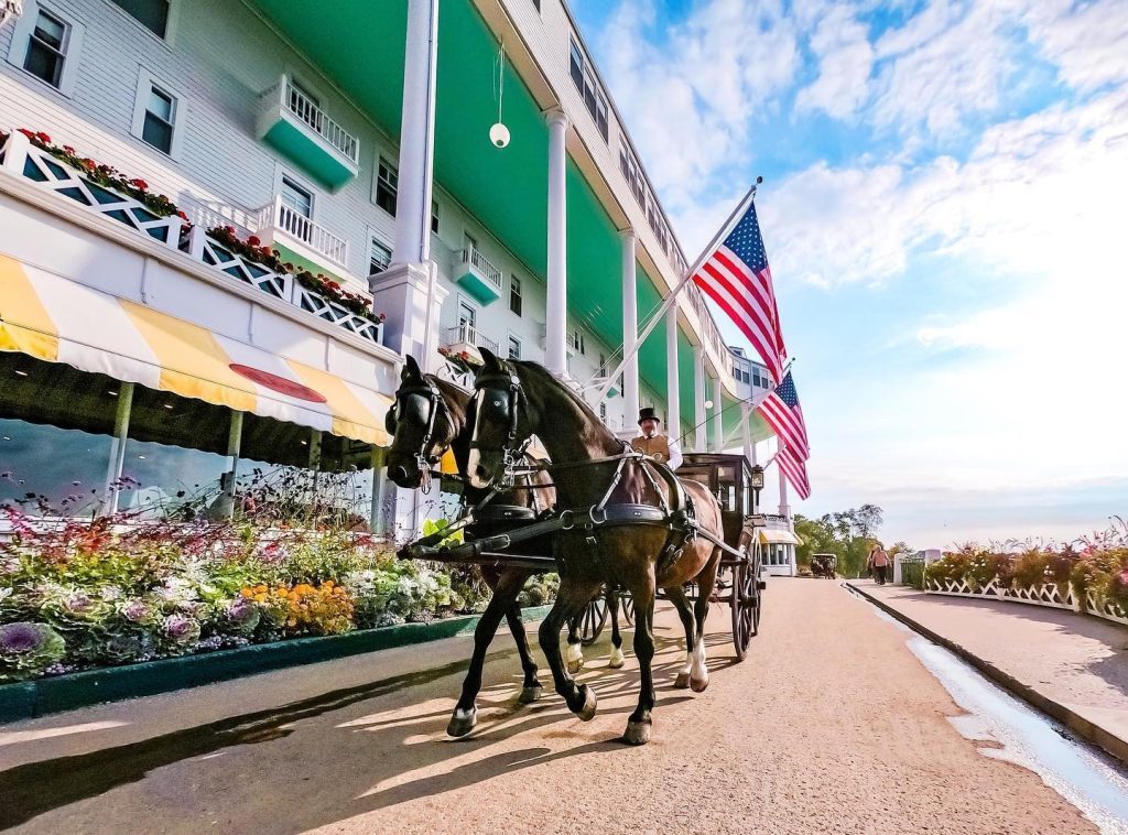 A private horse-drawn carriage passes in front of Mackinac Island’s Grand Hotel lined with flowers and American flags