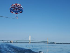 Mackinac Island parasailers float high above the water behind a speedboat with the Mackinac Bridge in the background