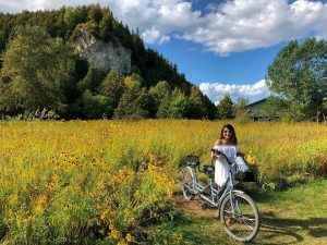 A young woman stands with a tandem bicycle in a field of wildflowers on Mackinac Island