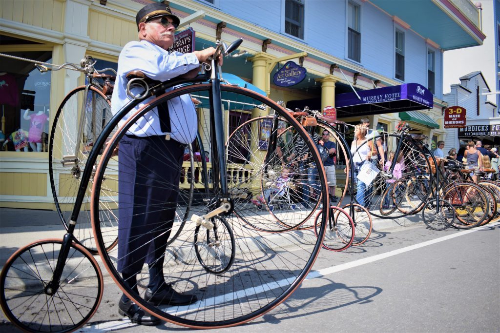 A man stands with a penny farthing bicycle on the street on Michigan's Mackinac Island