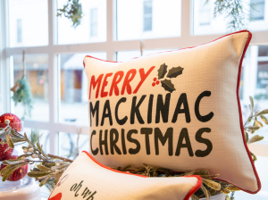 A storefront window in downtown Mackinac Island showcases a pillow with the words "Merry Mackinac Christmas"