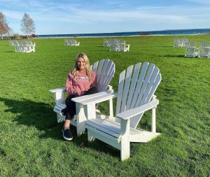 A woman sits in one of many white Adirondack chairs on the waterfront lawn at Mackinac Island's Mission Point Resort