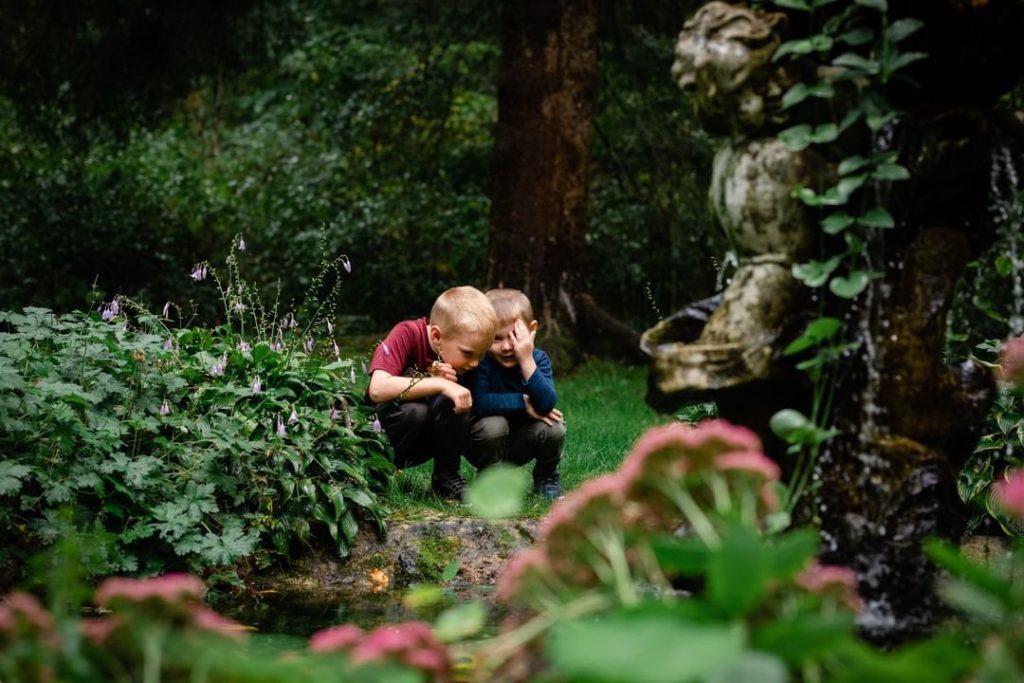 Two young boys whisper to each other while crouching near a tree on Mackinac Island