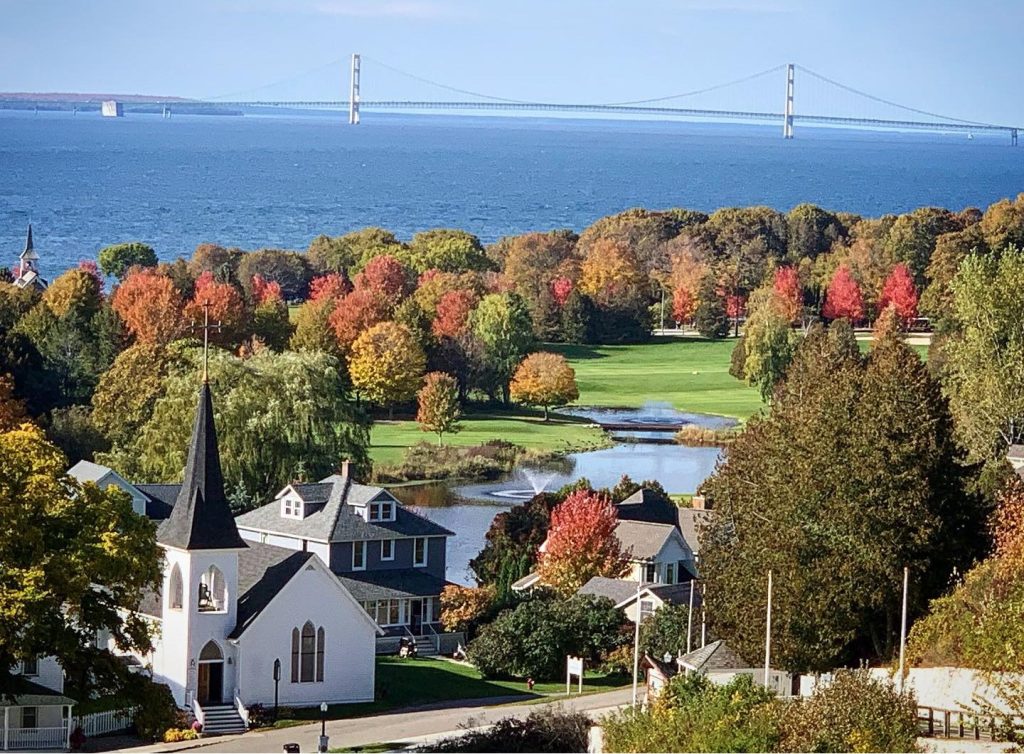 A view of Mackinac Island in the fall with leaf colors a church and the Mackinac Bridge