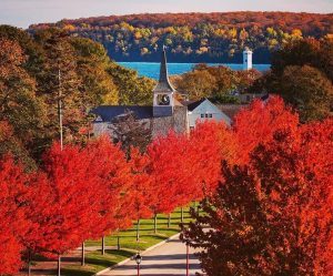 Bright red trees line a street on Mackinac Island with a church building and lighthouse in the background