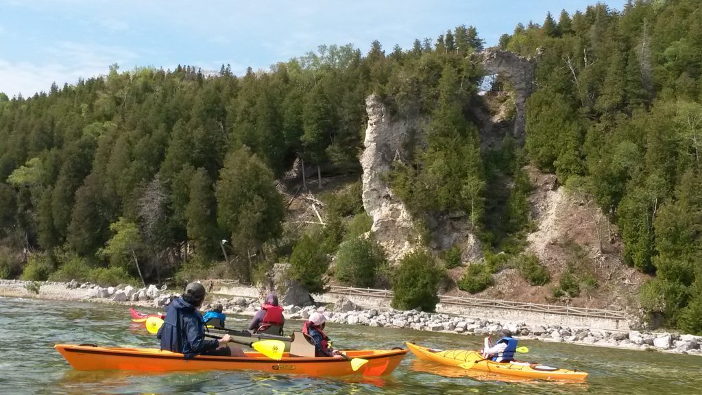 A flotilla of kayaks in Lake Huron pauses off Mackinac Island beneath Arch Rock