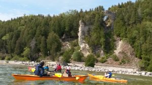 A group of paddlers steady their kayaks to take pictures of Mackinac Island’s Arch Rock from the water below