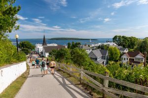 People walk downhill on a Mackinac Island street overlooking downtown and the water beyond