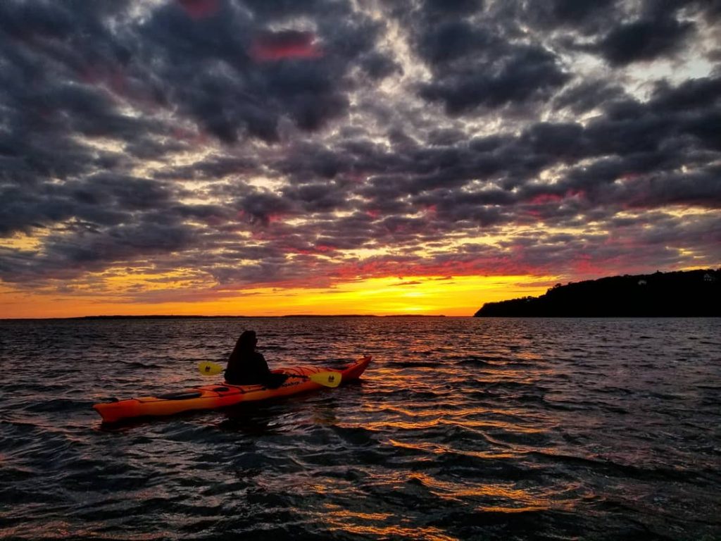 A paddler in the water off Mackinac Island points a kayak toward the setting sun