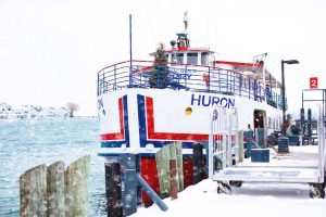 A Mackinac Island ferry boat with a Christmas tree in the bow pulls into the dock on a snowy winter day